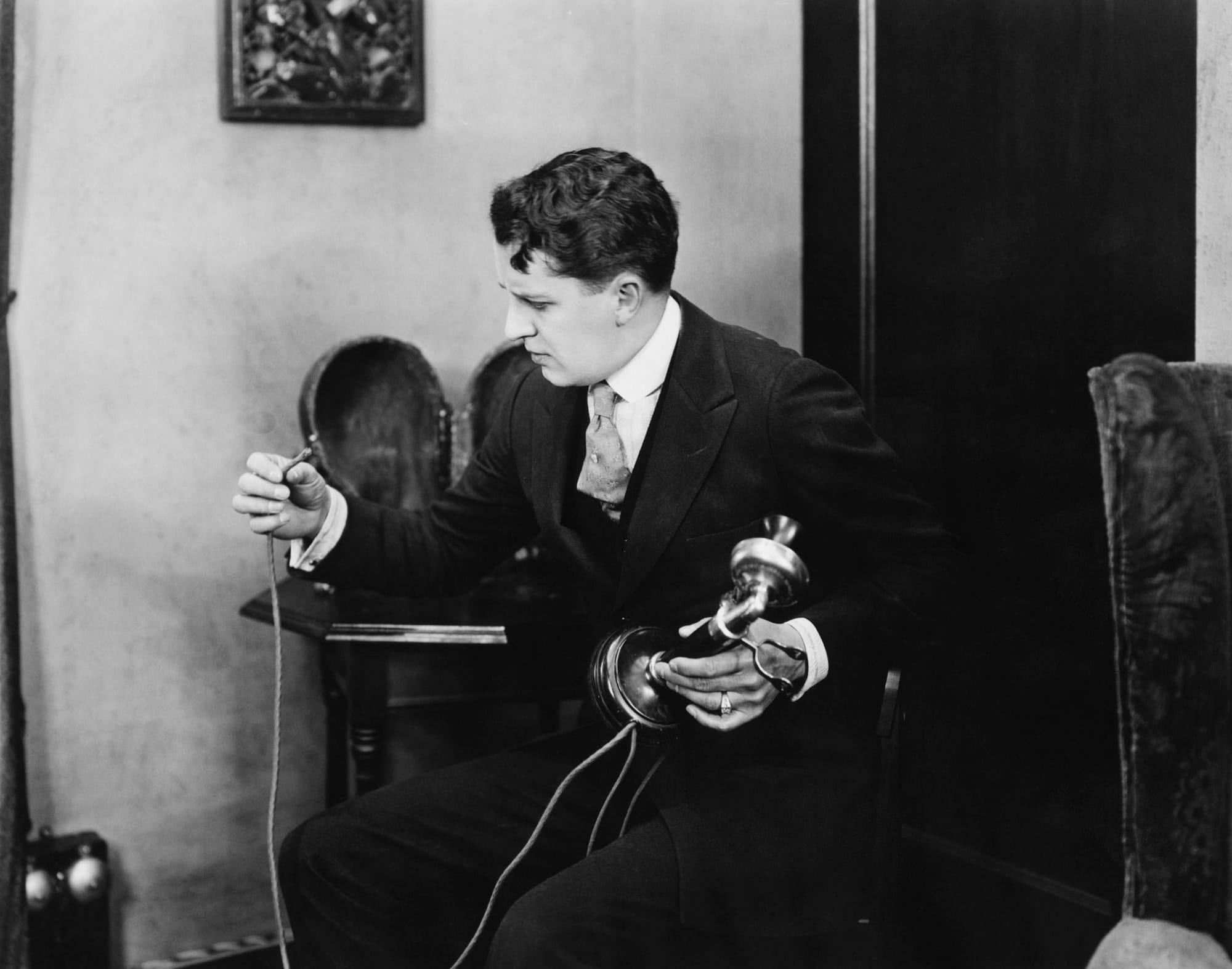 A man examines a severed cord on an early candlestick telephone.